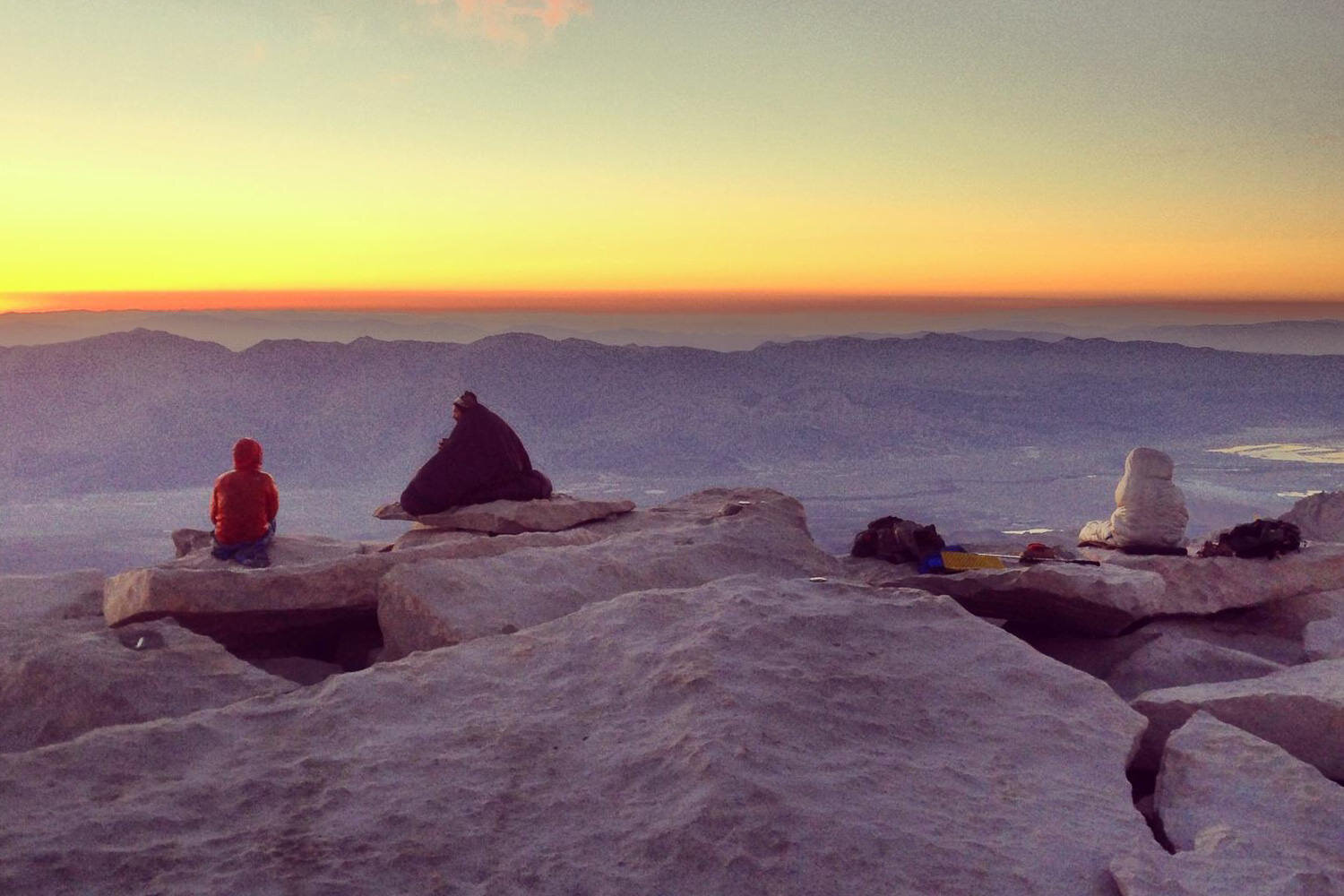 Hikers “wear” their sleeping bags to watch the sunrise at the summit of Mt. Whitney