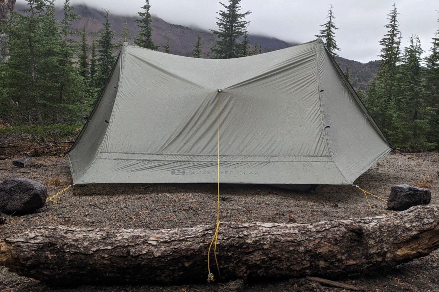 The Gossamer Gear The Two set up in front of a foggy mountain with guylines tied off to a log and some rocks