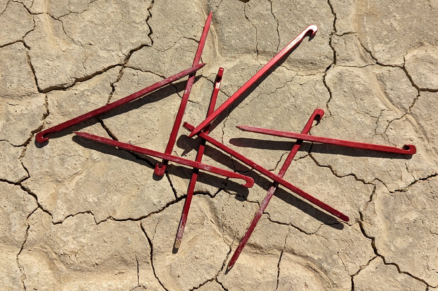 A pile of thin red stakes laying slopshod on the ground.
