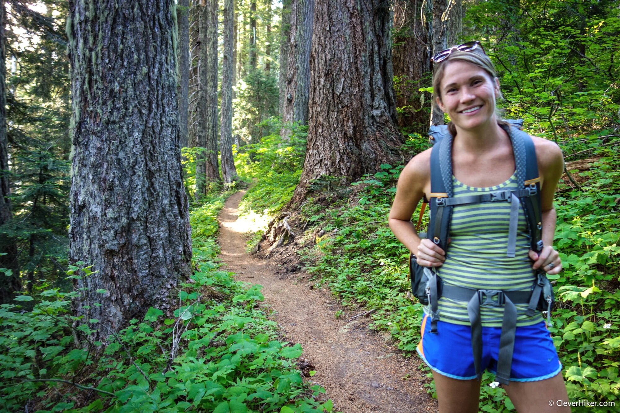 A hiker training for a backpacking trip in the woods with a trail in the background