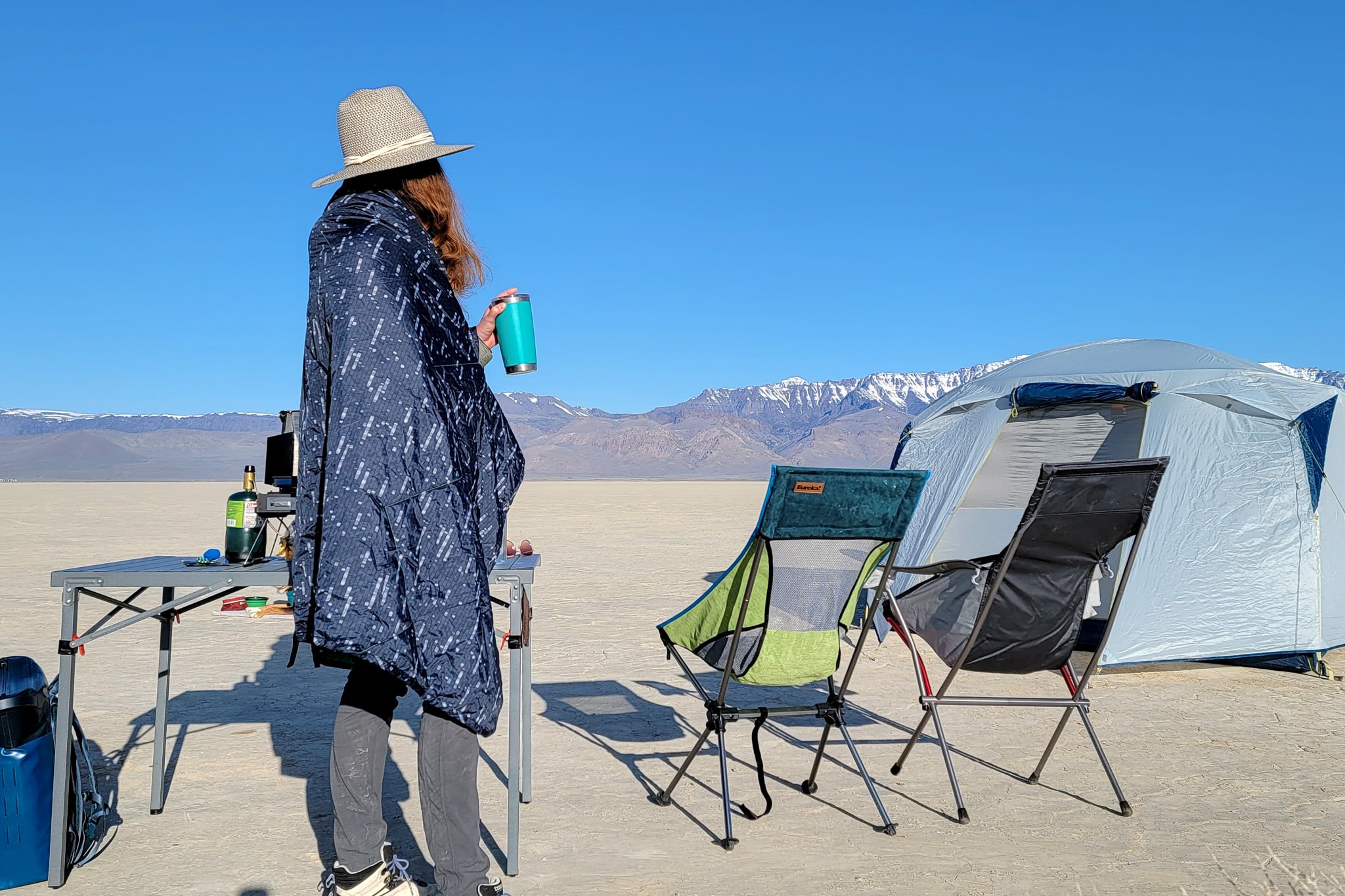 A person standing in a campsite in the desert wrapped up in a camp blanket