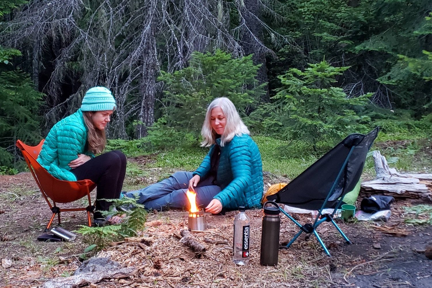 Two people in a forest sitting next to a fire in the Solo Stove Campfire Stove