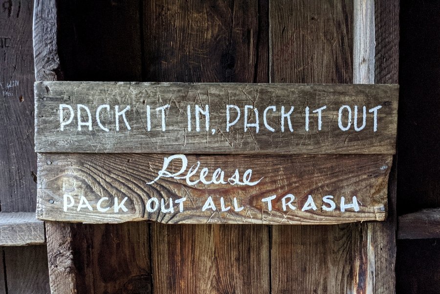 A wooden sign that reads pack it in pack it out please pack out all trash
