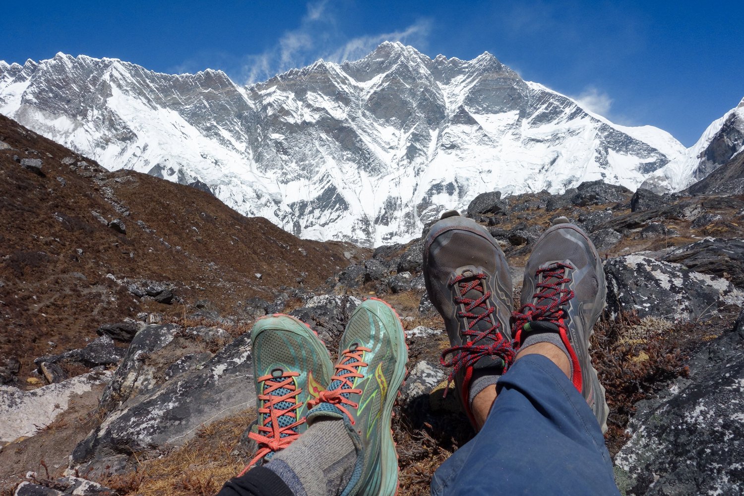 Two pairs of feet wearing Saucony Peregrine shoes in front of a mountain view