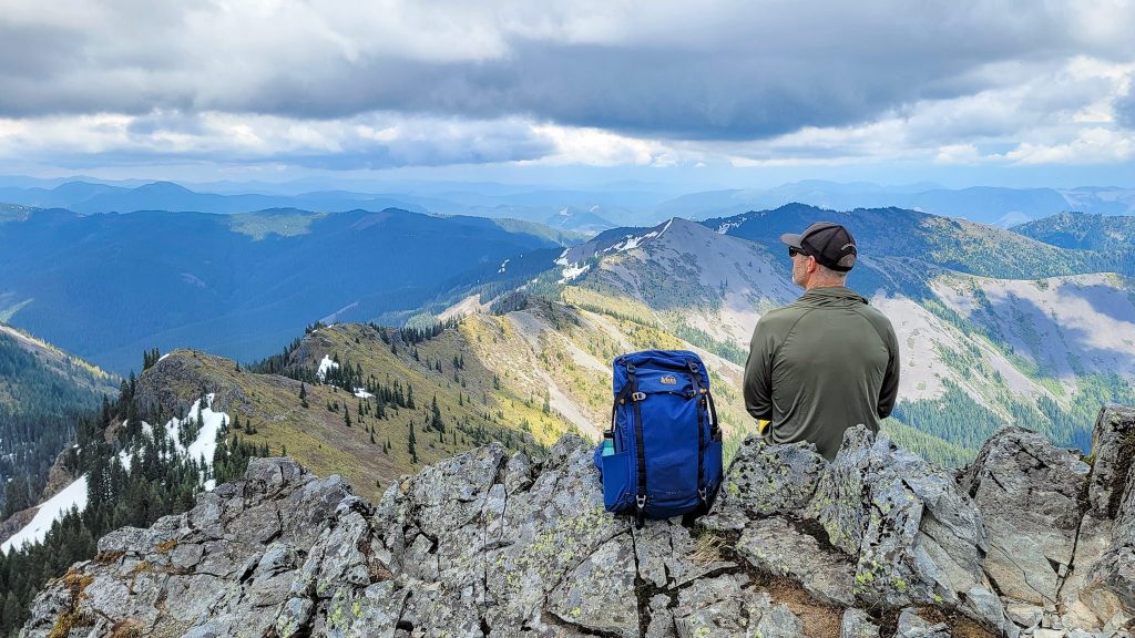 A hiker sitting next to the REI Trail 25 daypack on a mountain ridge