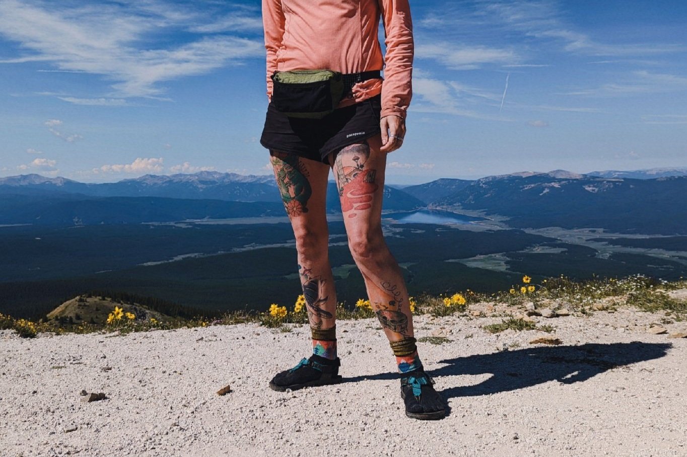 A torso down view of a hiker standing at the top of a mountain pass