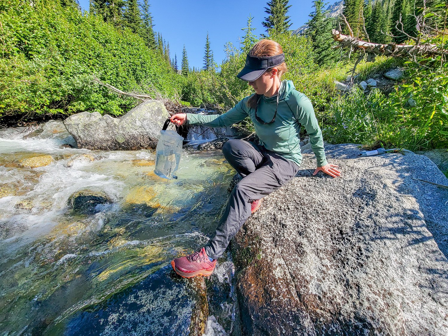 A backpacker dipping water from a creek with the Platypus GravityWorks Water Filter