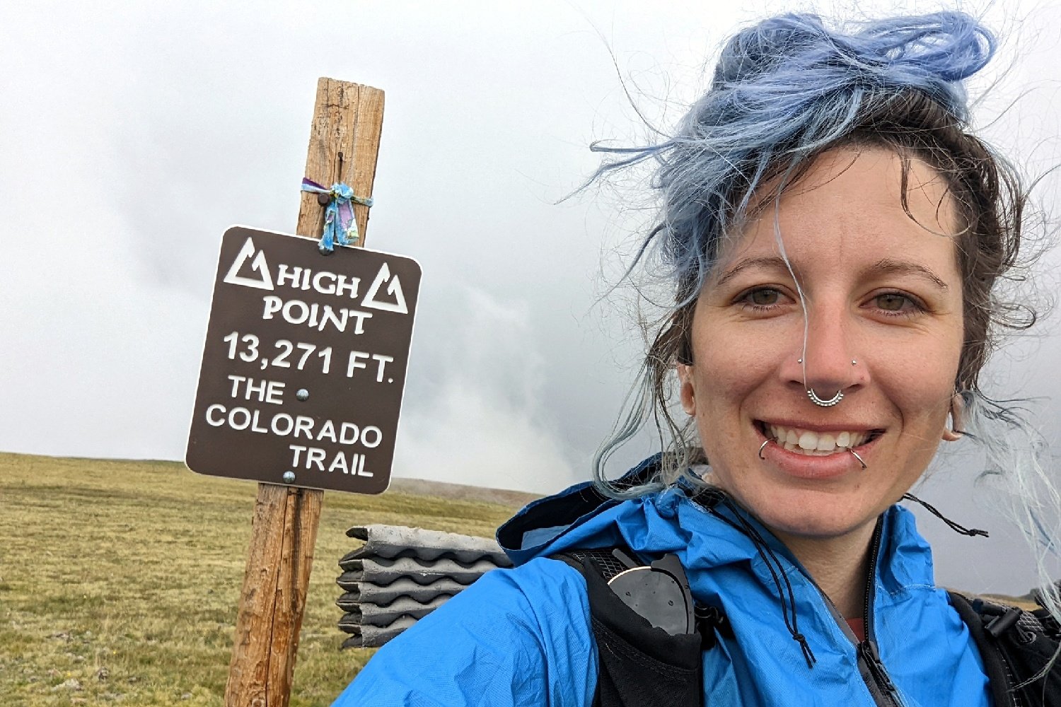 A selfie of a hiker with a sign marking the high point of the Colorado Trail