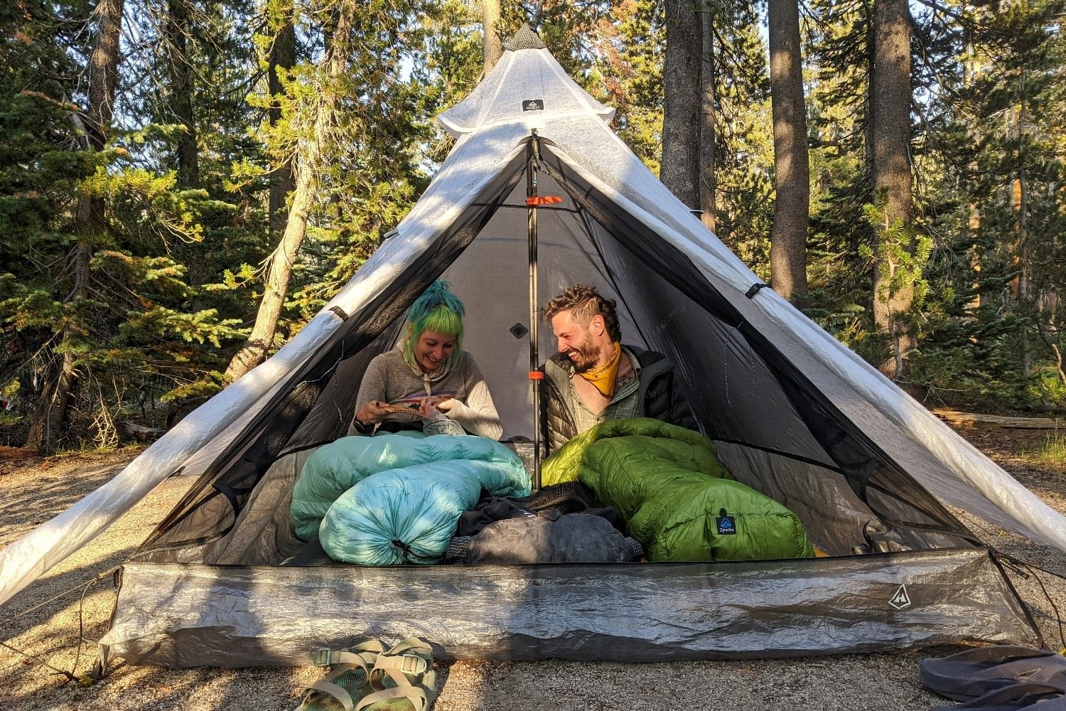 Two hikers sitting in backpacking quilts in a tent