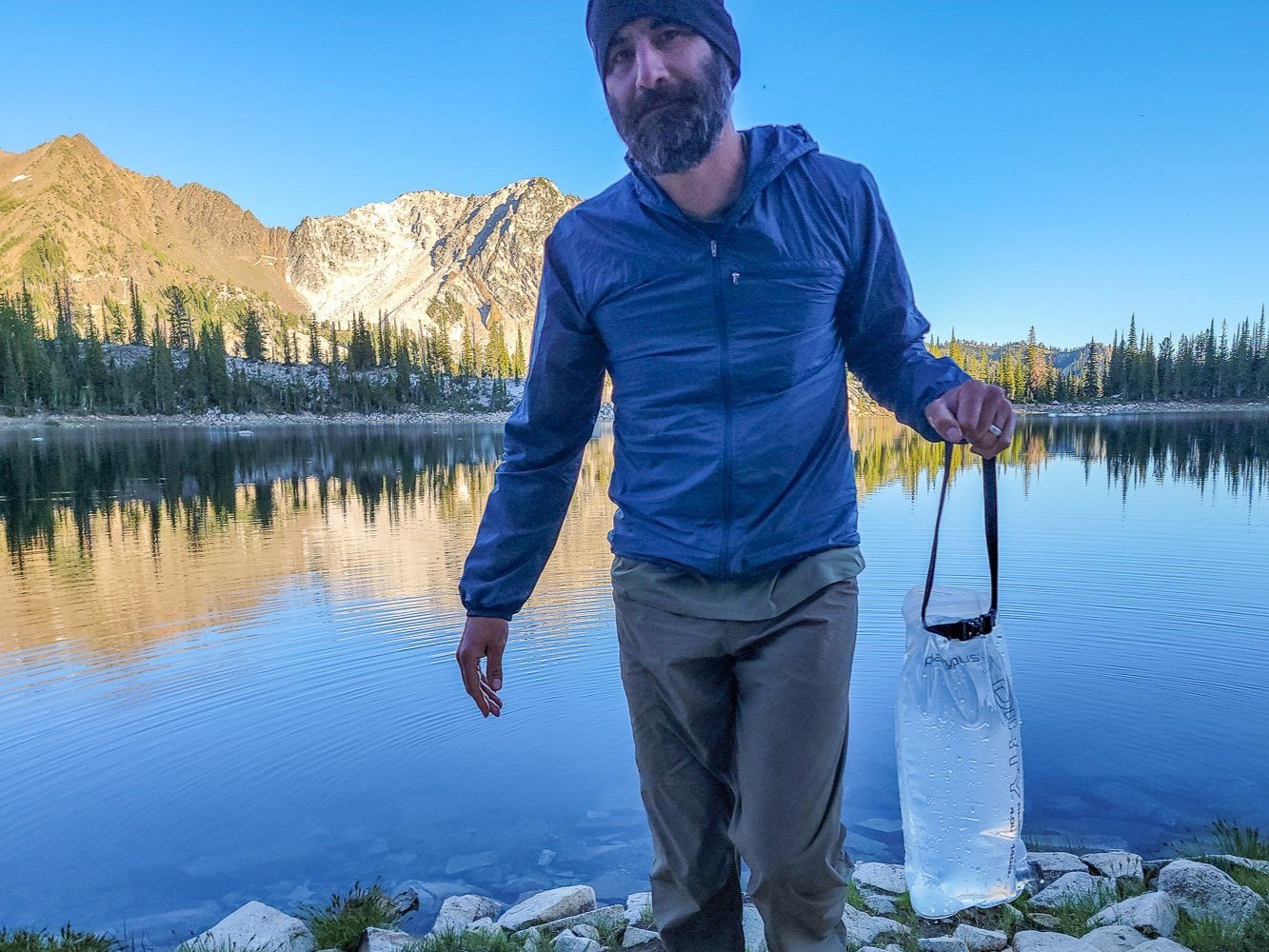 A backpacker getting water out of a lake with the Platypus GravityWorks Water Filter