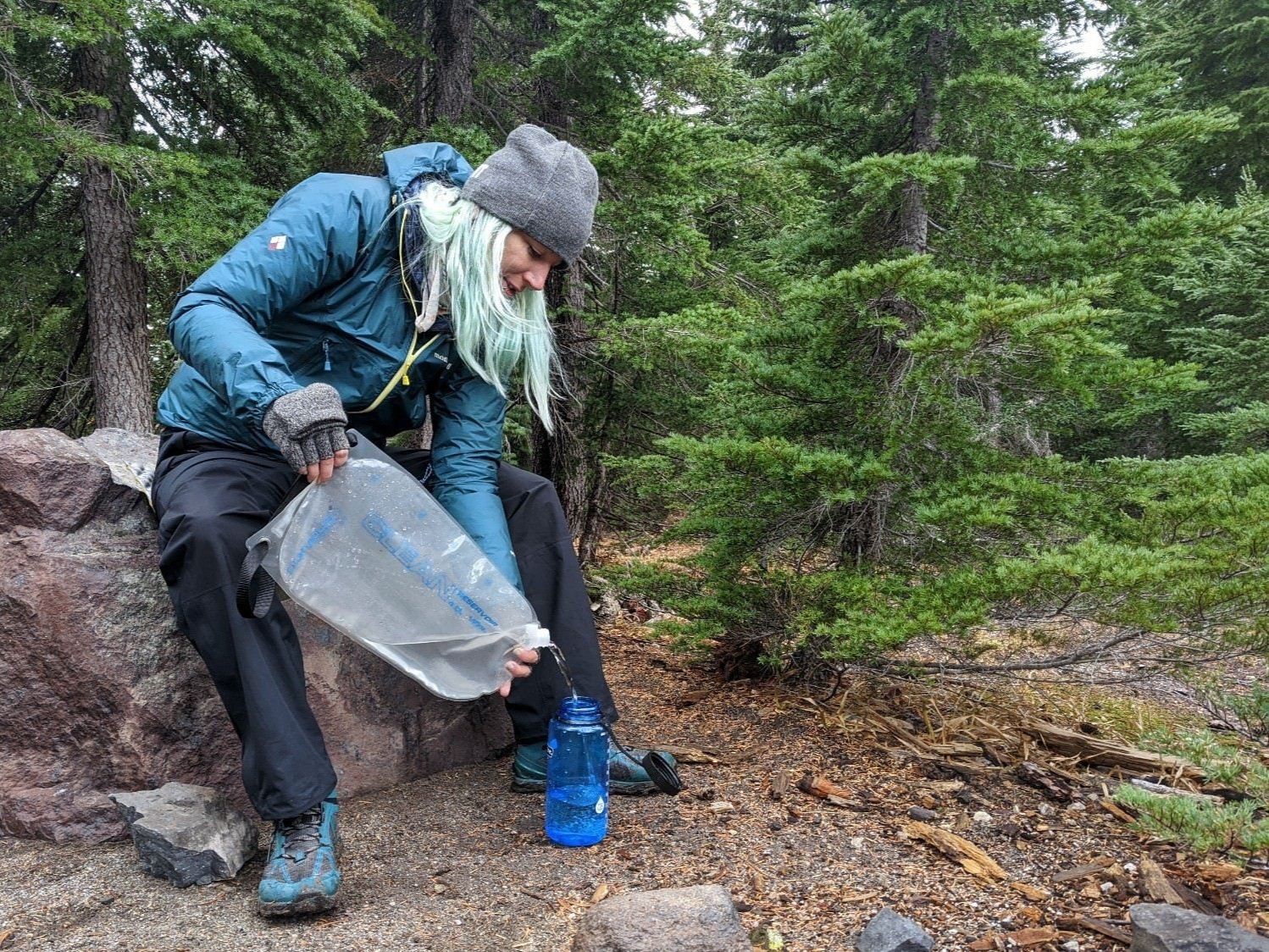 A backpacker pouring water into a water bottle from the clean reservoir of the Platypus GravityWorks Water Filter