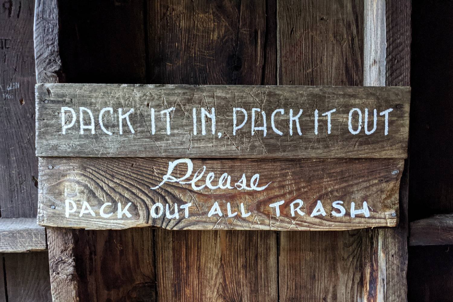 A wooden sign that says pack it in pack it out please pack out all trash