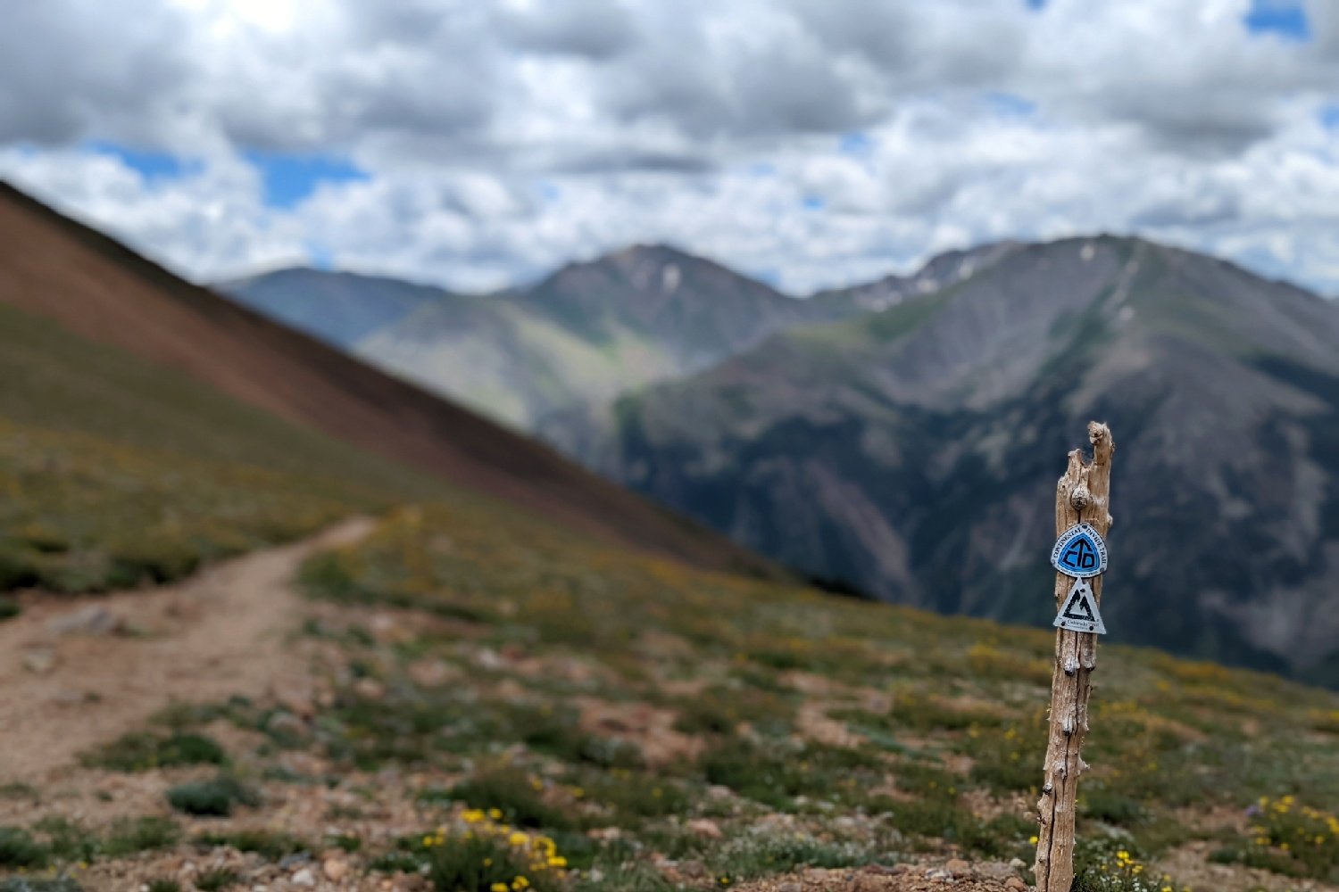 A post marking the path of the Continental Divide and Colorado Trails with mountains in the background