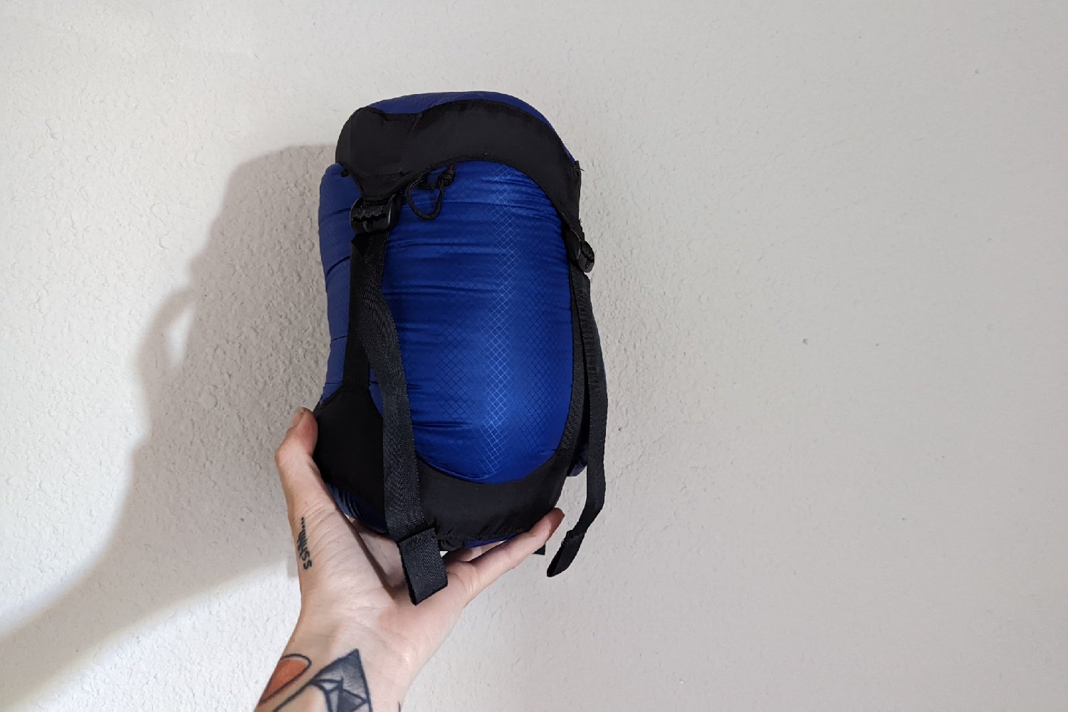 A person holding up a compression sack with the Zpacks Classic Sleeping Bag inside in front of a white background