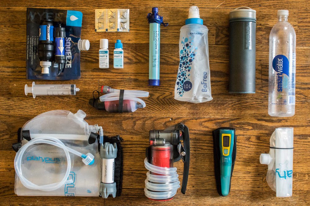 A variety of backpacking water filters and purifiers laid out on a table for size comparison