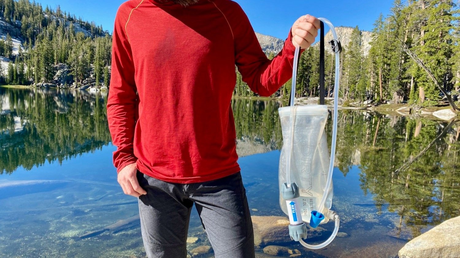Closeup of a backpacker holding the Platypus GravityWorks Water Filter in front of a lake