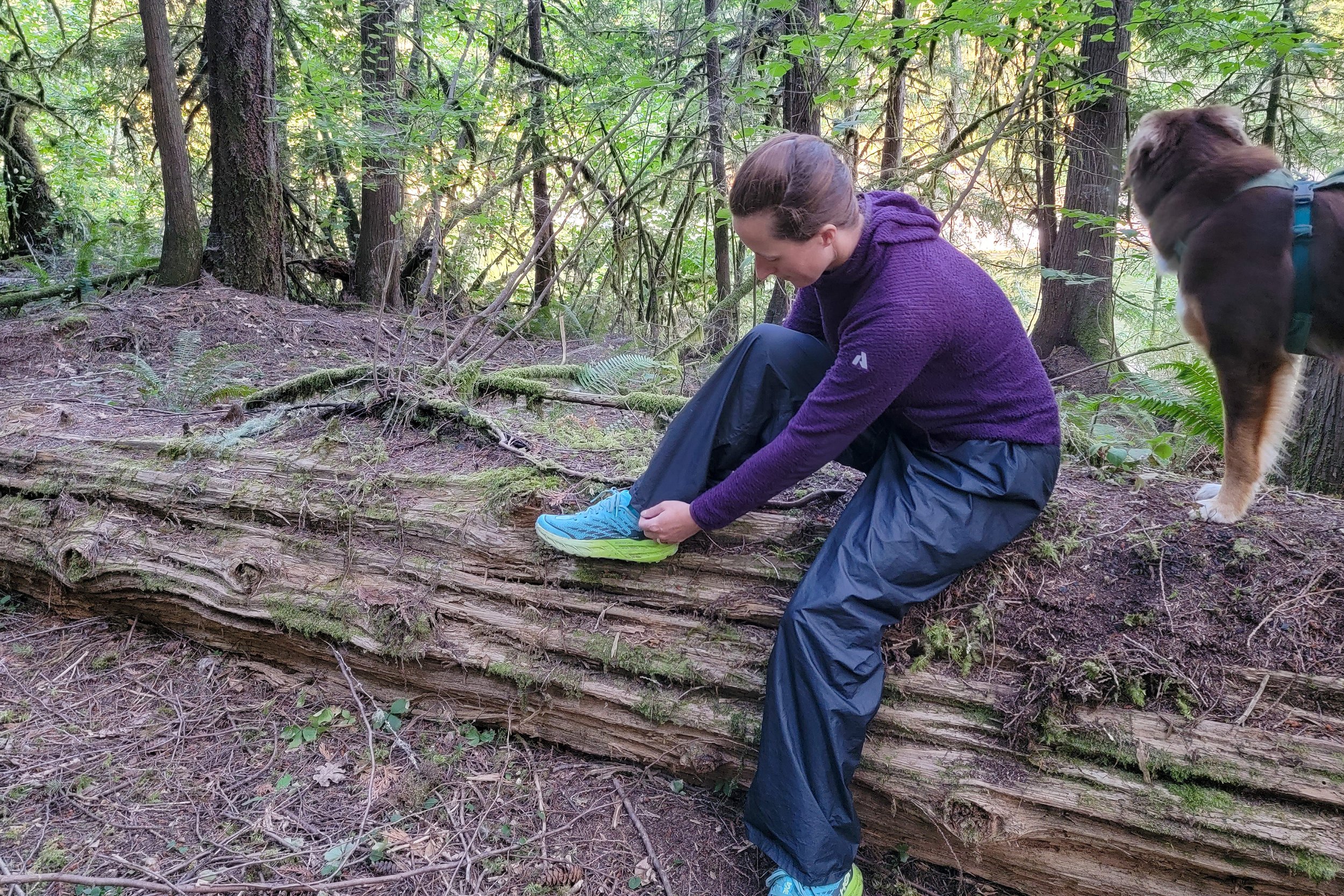 A hiker sitting on a log putting on the Zpacks Vertice Rain Pants