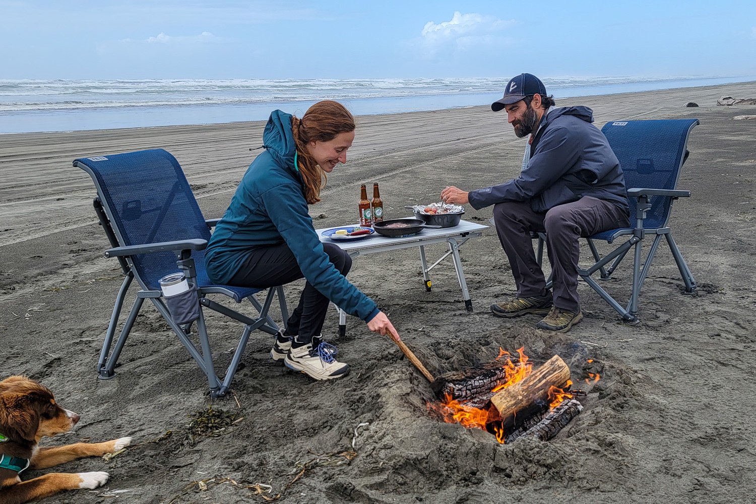 A couple using the YETI Trailhead Camp Chair while cooking over a fire on the beach