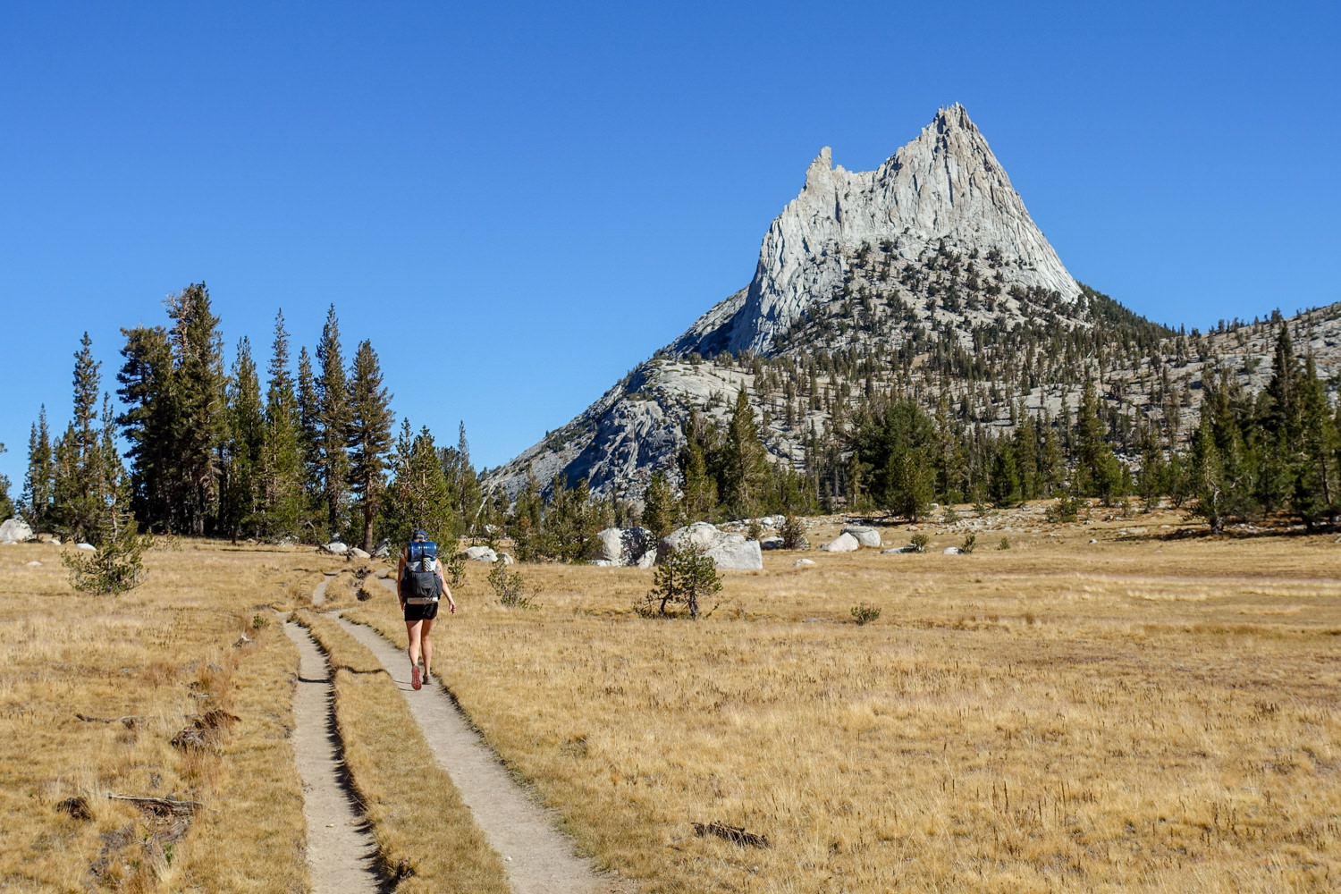 Backpacker walking towards a granite spire on the John Muir Trail