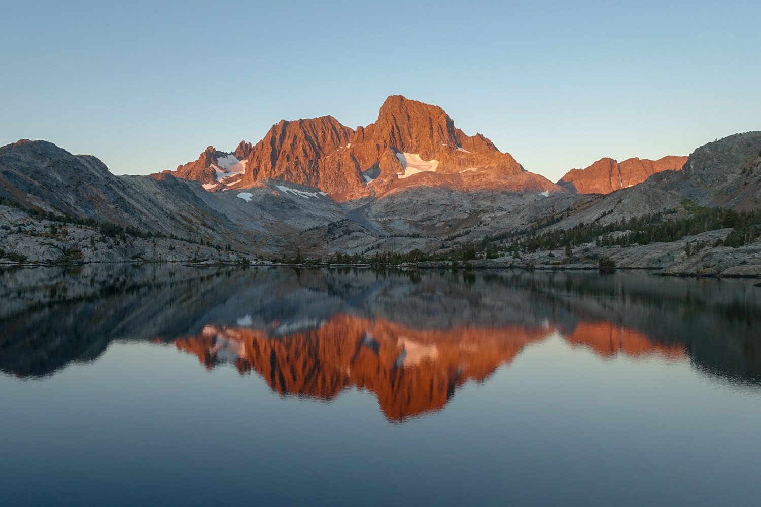 sunset alpenglow on a craggy peak reflecting on a still lake