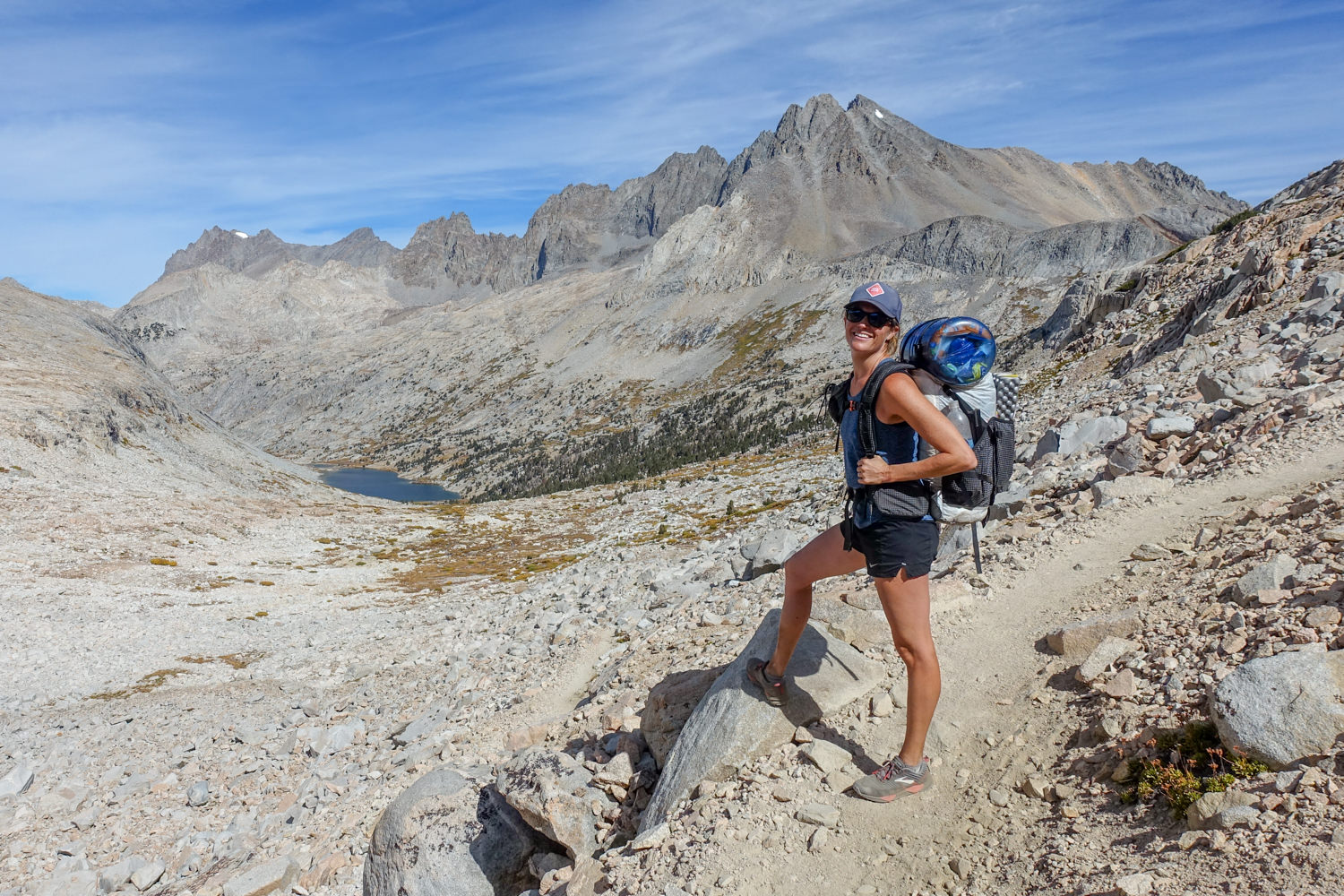 backpacker on the john muir trail posing above a mountain basin and alpine lake in the sun