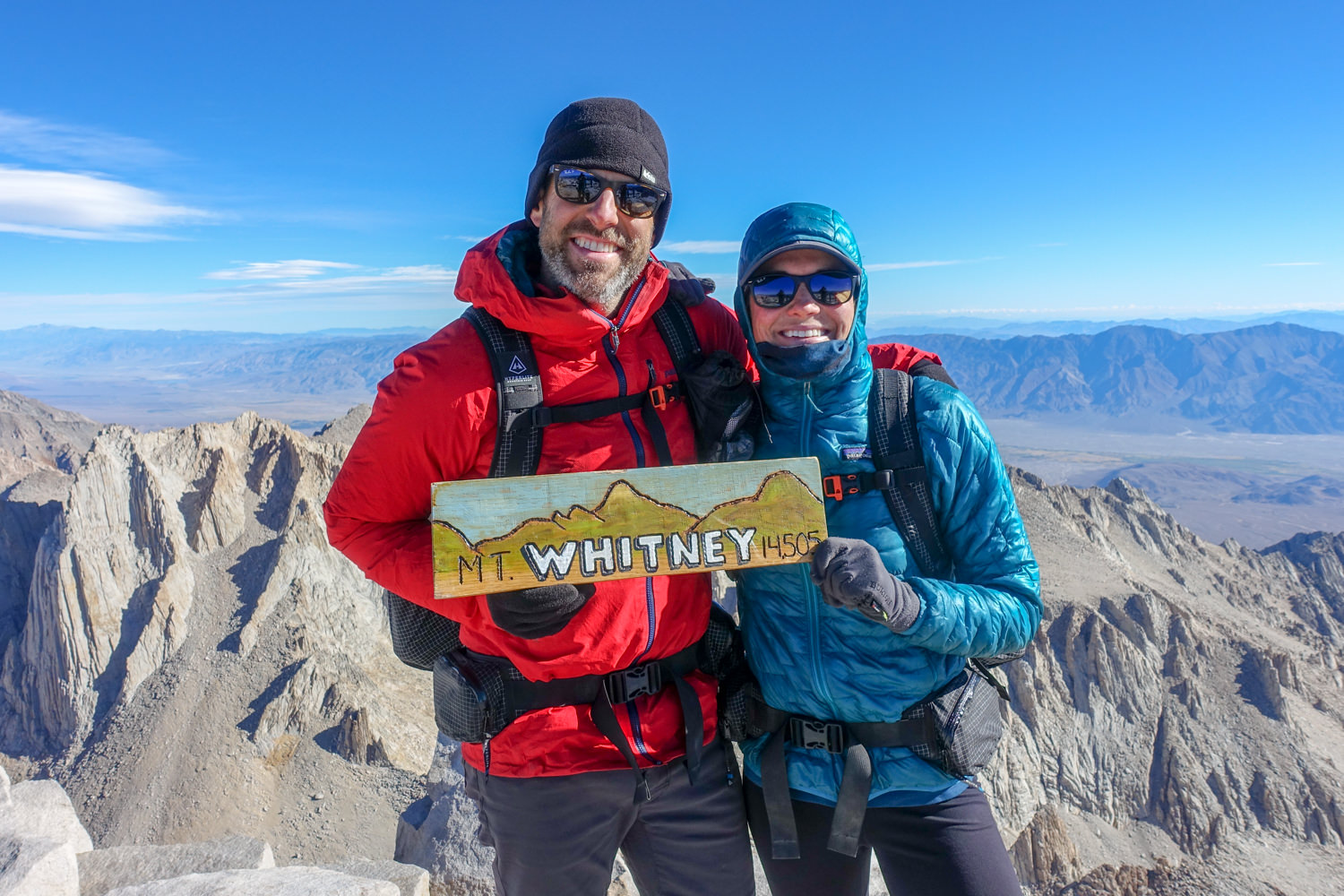 two backpackers on the summit of mount whitney holding up a hand painted sign that says Mt. Whitney