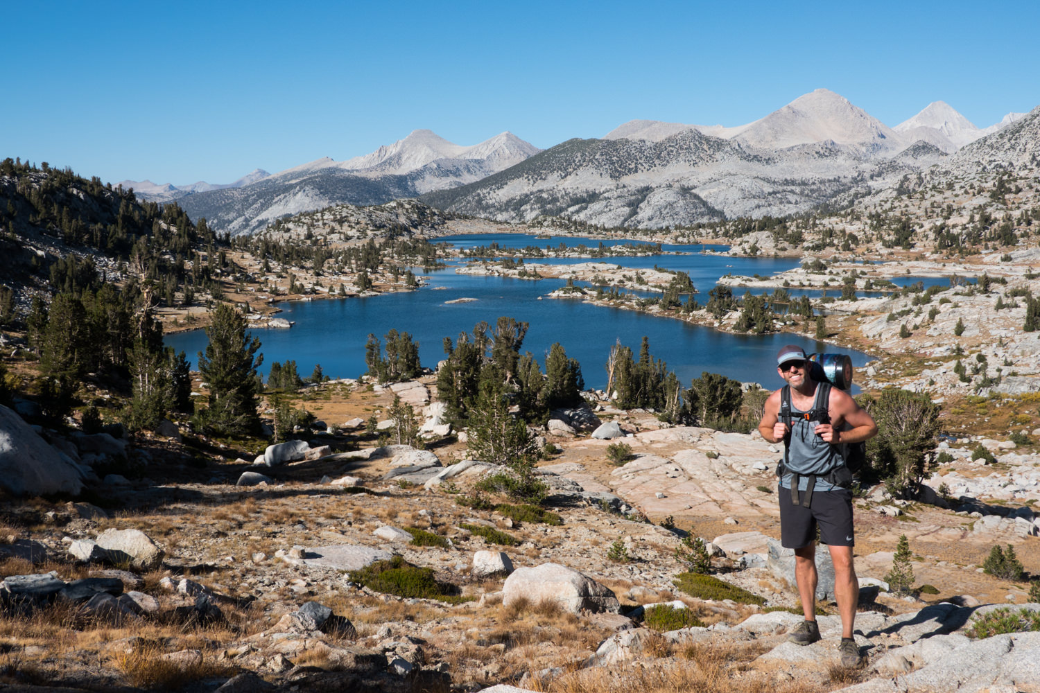 Backpacker posing in front of two alpine lakes on a sunny day