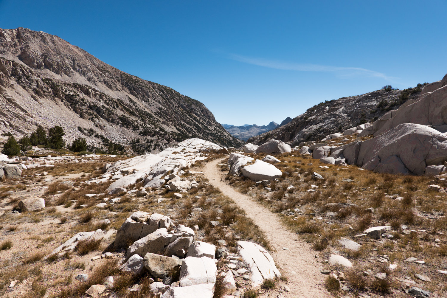 Wide trail dissapears from view as the mountains create a valley on either side of it.