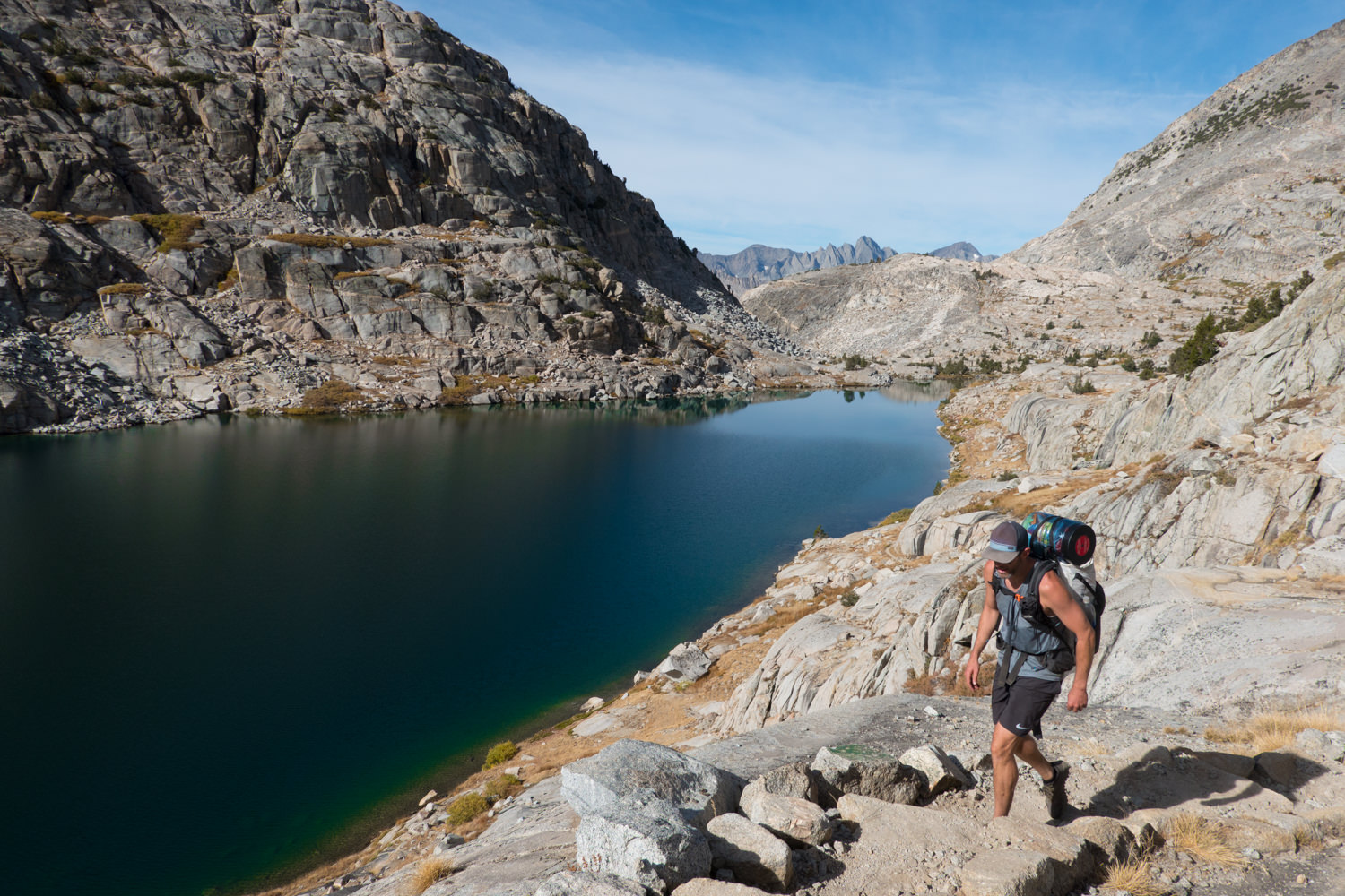 Backpacker on the JMT hiking along a deep blue lake.