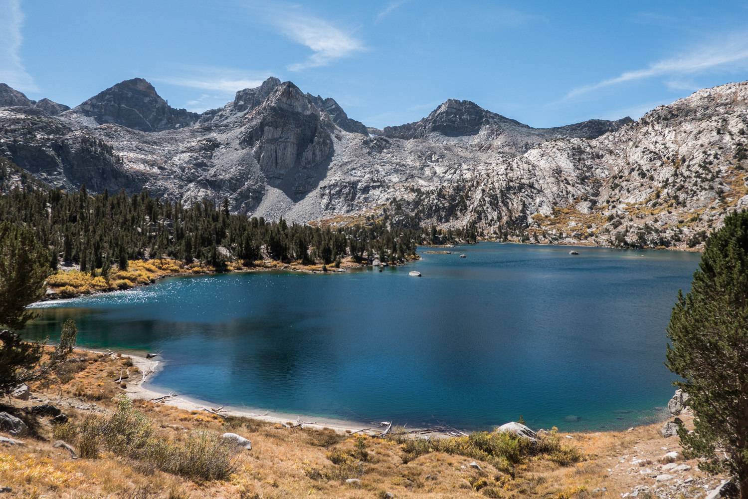 large alpine lake with sand pebble shoreline and mountains in the background