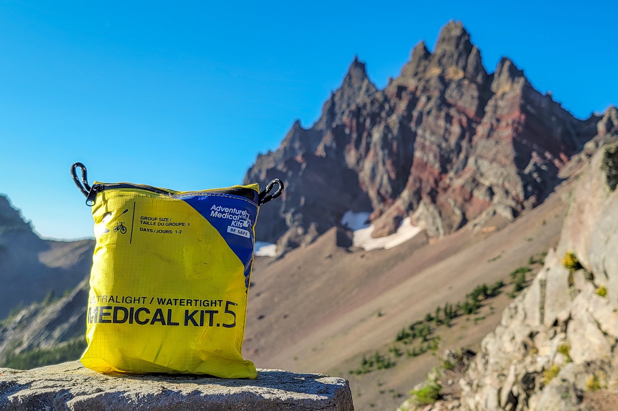 An Adventure Medical Kits First Aid Kit sitting on a rock in front of a mountain view