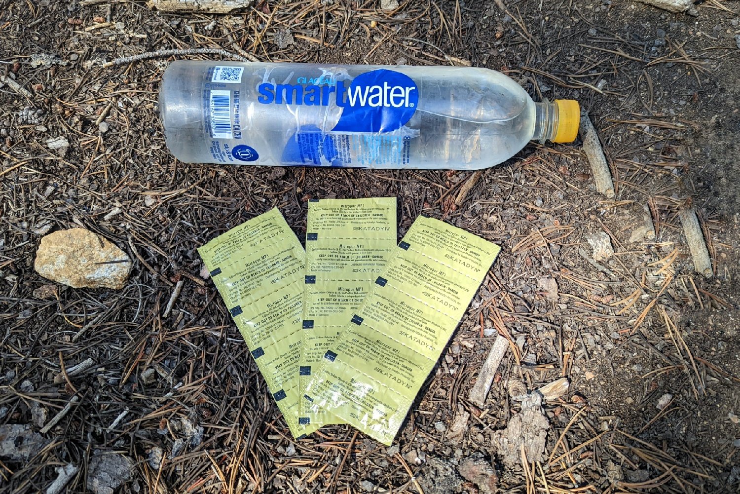 Packets of Katadyn Micropur Tabs laying on the ground in front of a Smartwater bottle