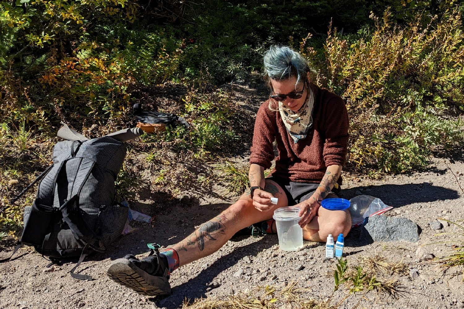 A hiker dropping Aquamira treatment into a water bottle on trail