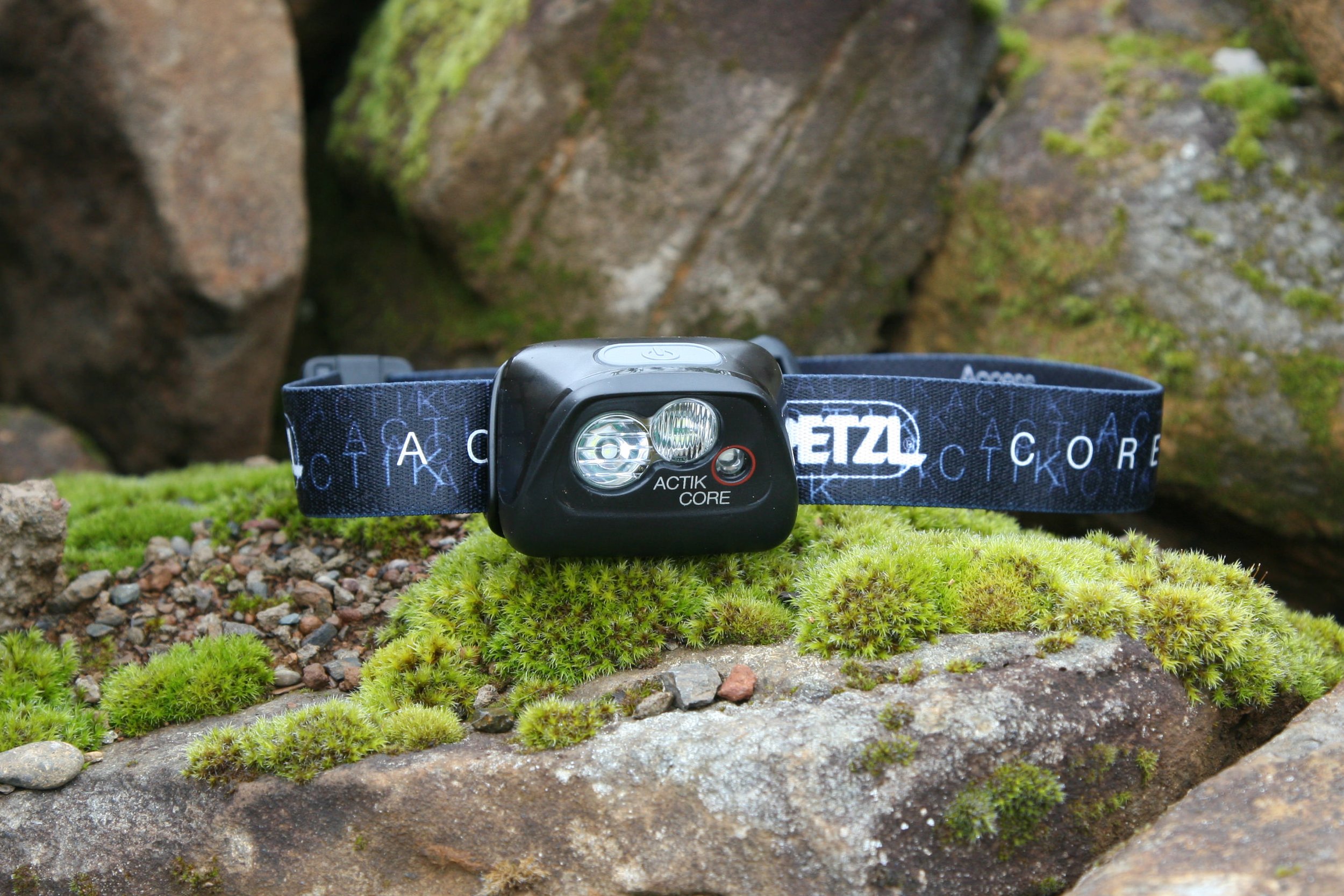 A Petzl Actik Core headlamp sitting on a mossy rock