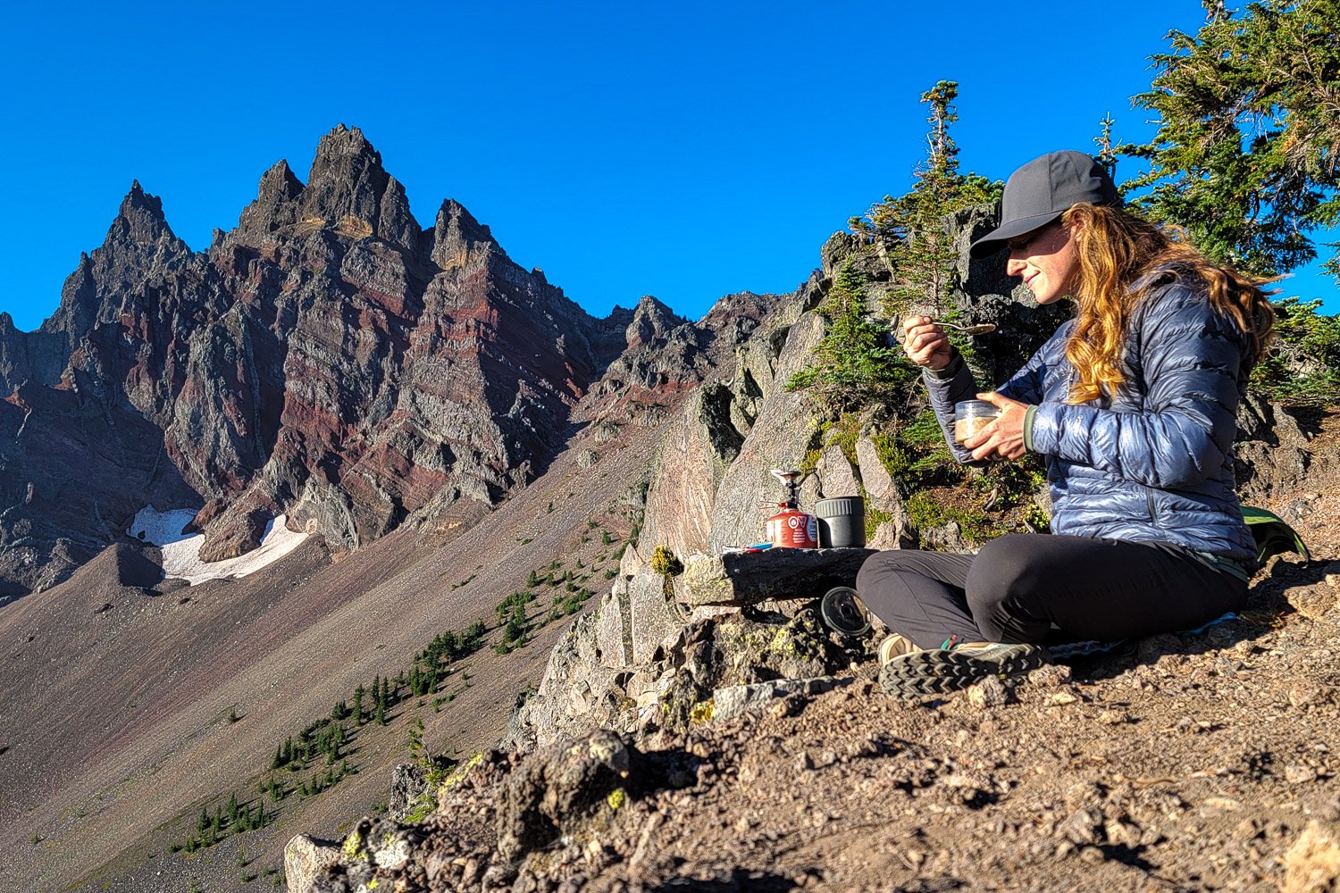 A backpacker eating a meal near a craggy mountain peak