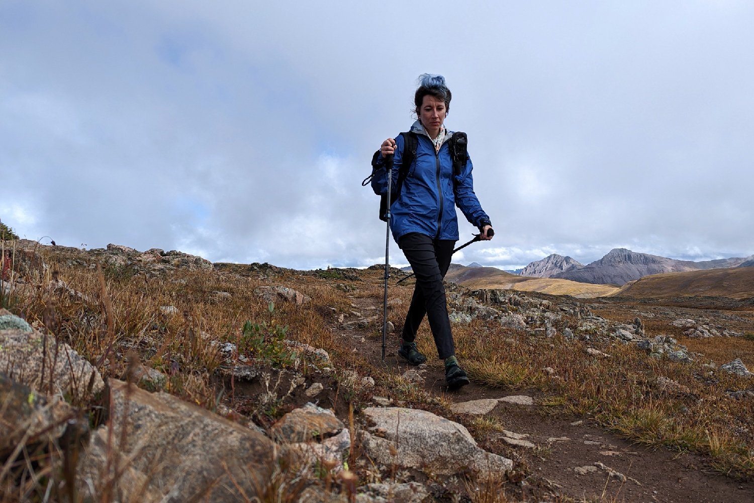 A hiker wearing the Enlightened Equipment Visp rain jacket on a rainy mountain pass