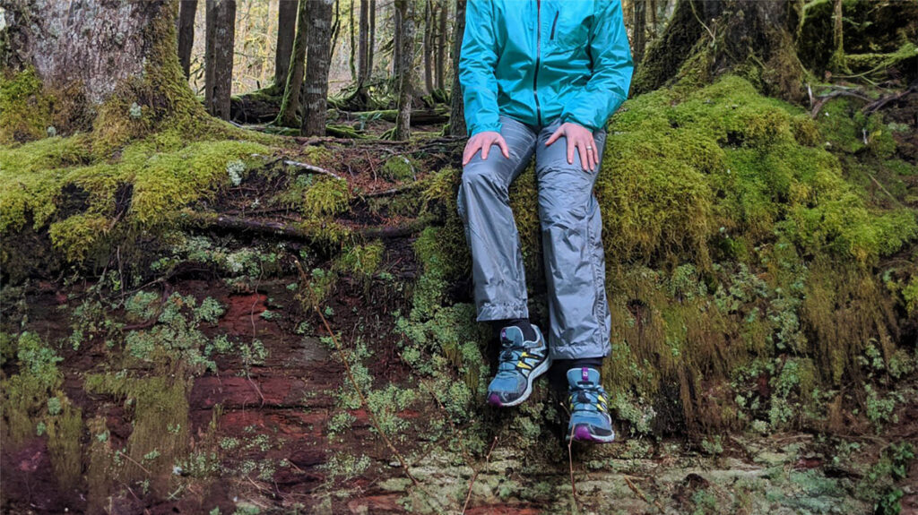 A hiker sitting on a mossy old growth log in the Outdoor Research Helium Rain Pants