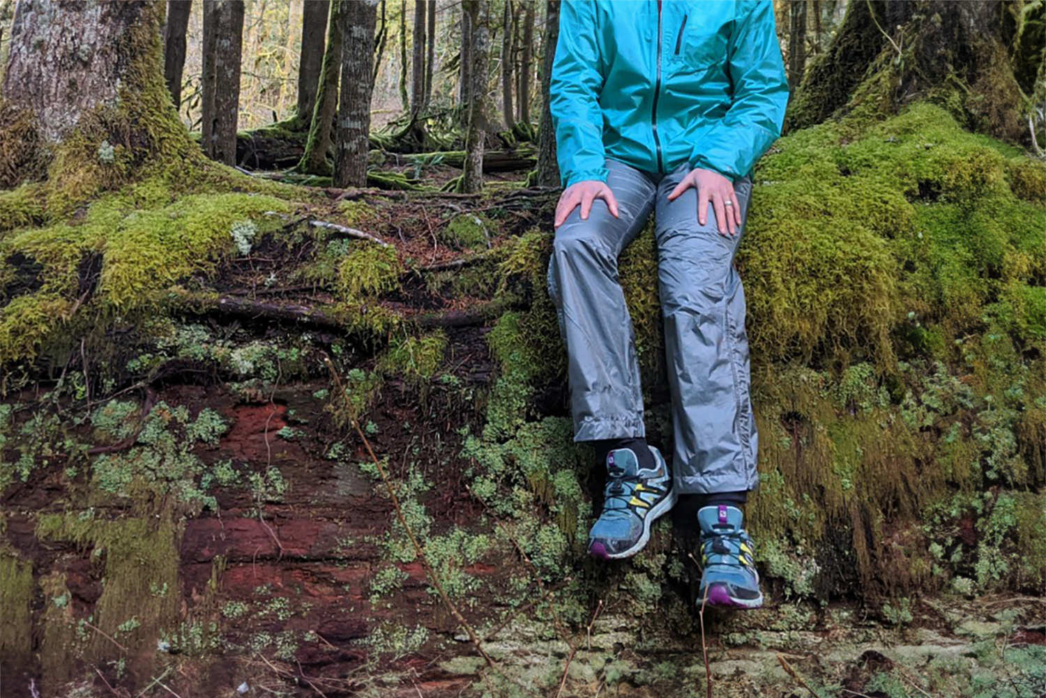A hiker sitting on a mossy old growth log in the Outdoor Research Helium Rain Pants
