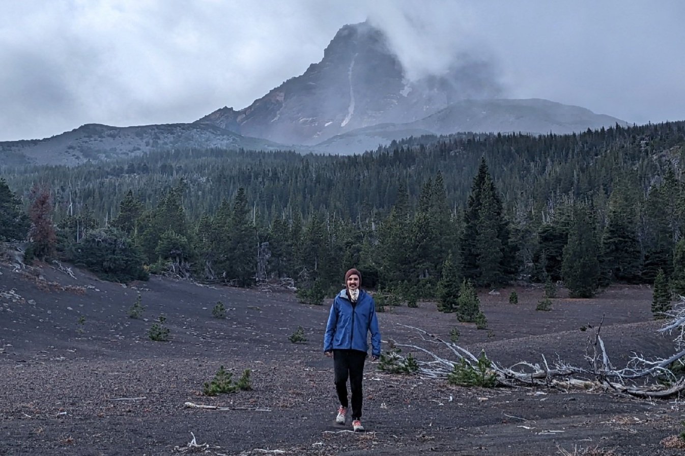 A hiker wearing the Enlightened Equipment Visp in front of a mountain view