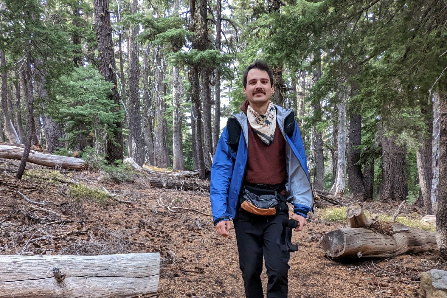 A hiker walking on a trail wearing the Enlightened Equipment Visp rain jacket unzipped