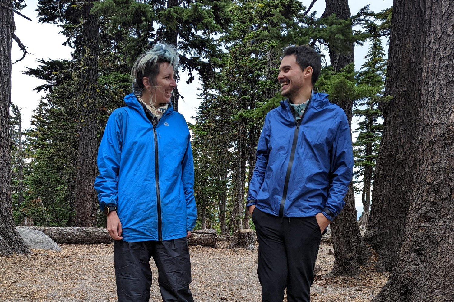 Two hikers wearing the Zpacks Vertice and the Enlightened Equipment Visp smiling at each other in a campsite