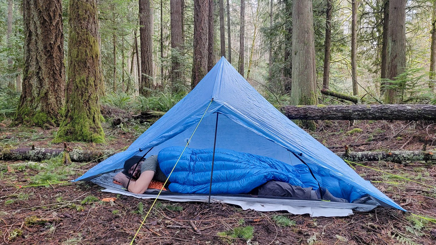 A backpacker using the Zpacks Mummy Bag as a quilt in a backpacking tent