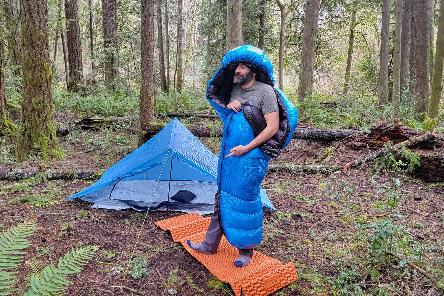 A hiker standing up with the bottom of the Zpacks Mummy Bag unzipped to demonstrate the zip-around footbox