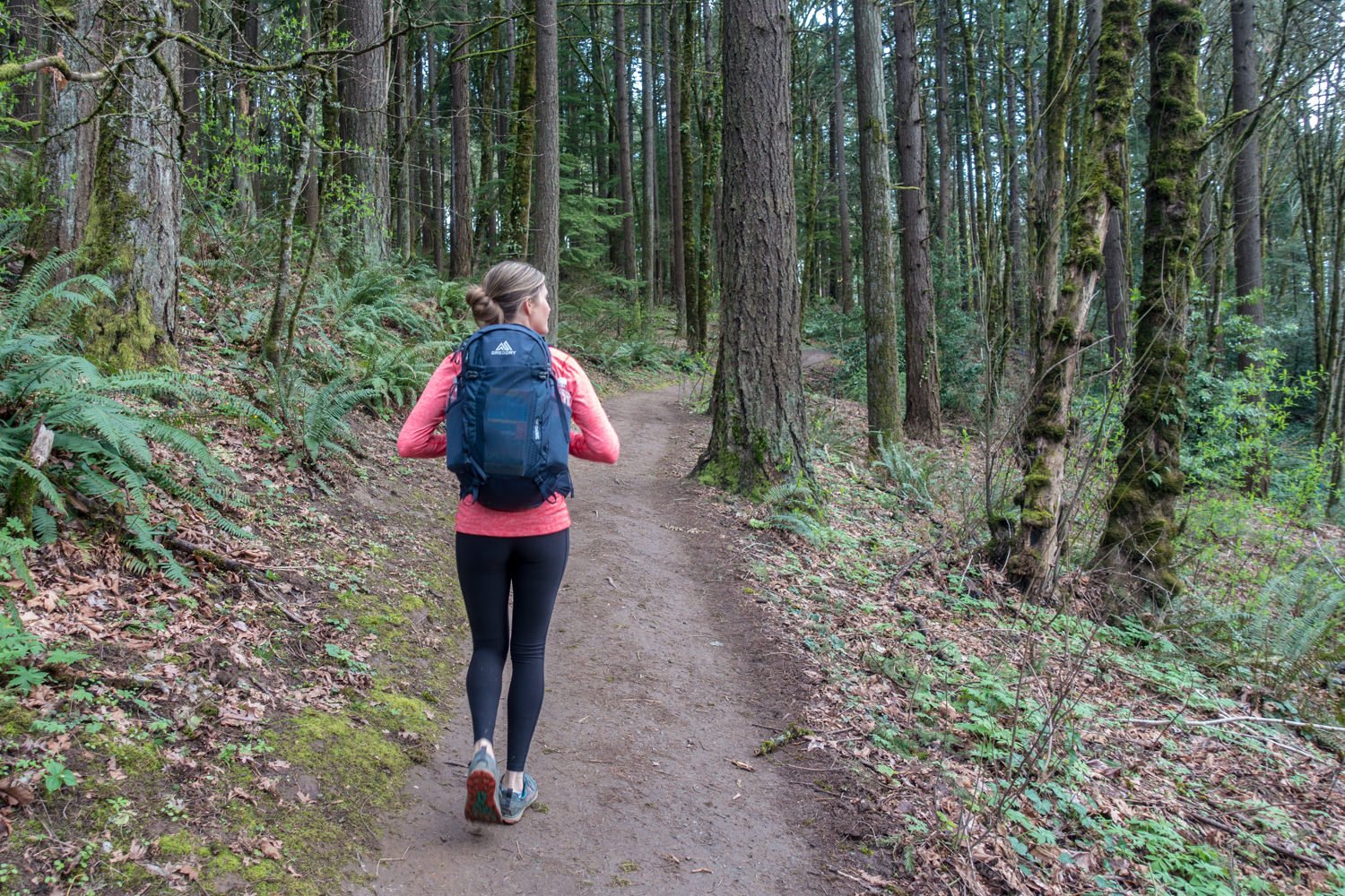 A female hiker with a daypack walking down a path in the woods