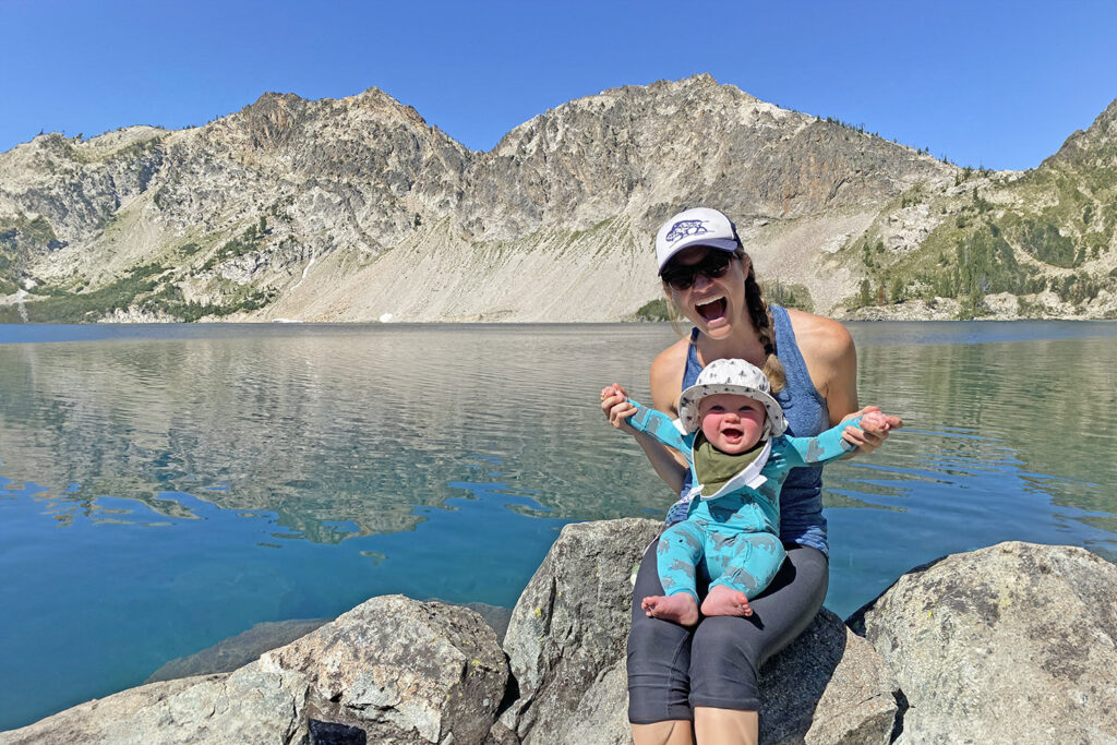 A mom posing with her baby in front of an alpine lake