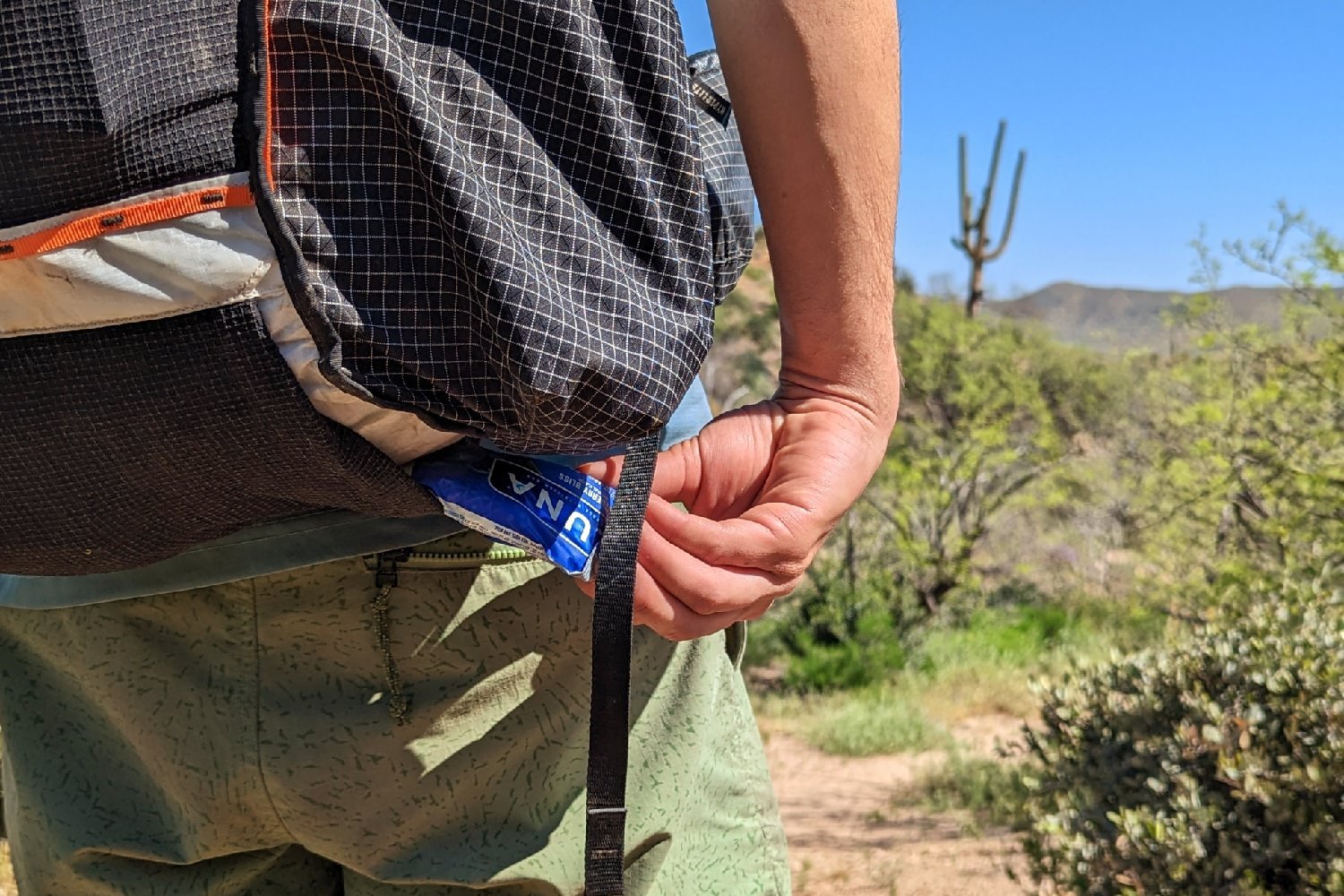 a close-up of a hikers hand pulling a luna bar out of the bottom pocket of the Hyperlite Mountain Gear Unbound 40 in a desert scene