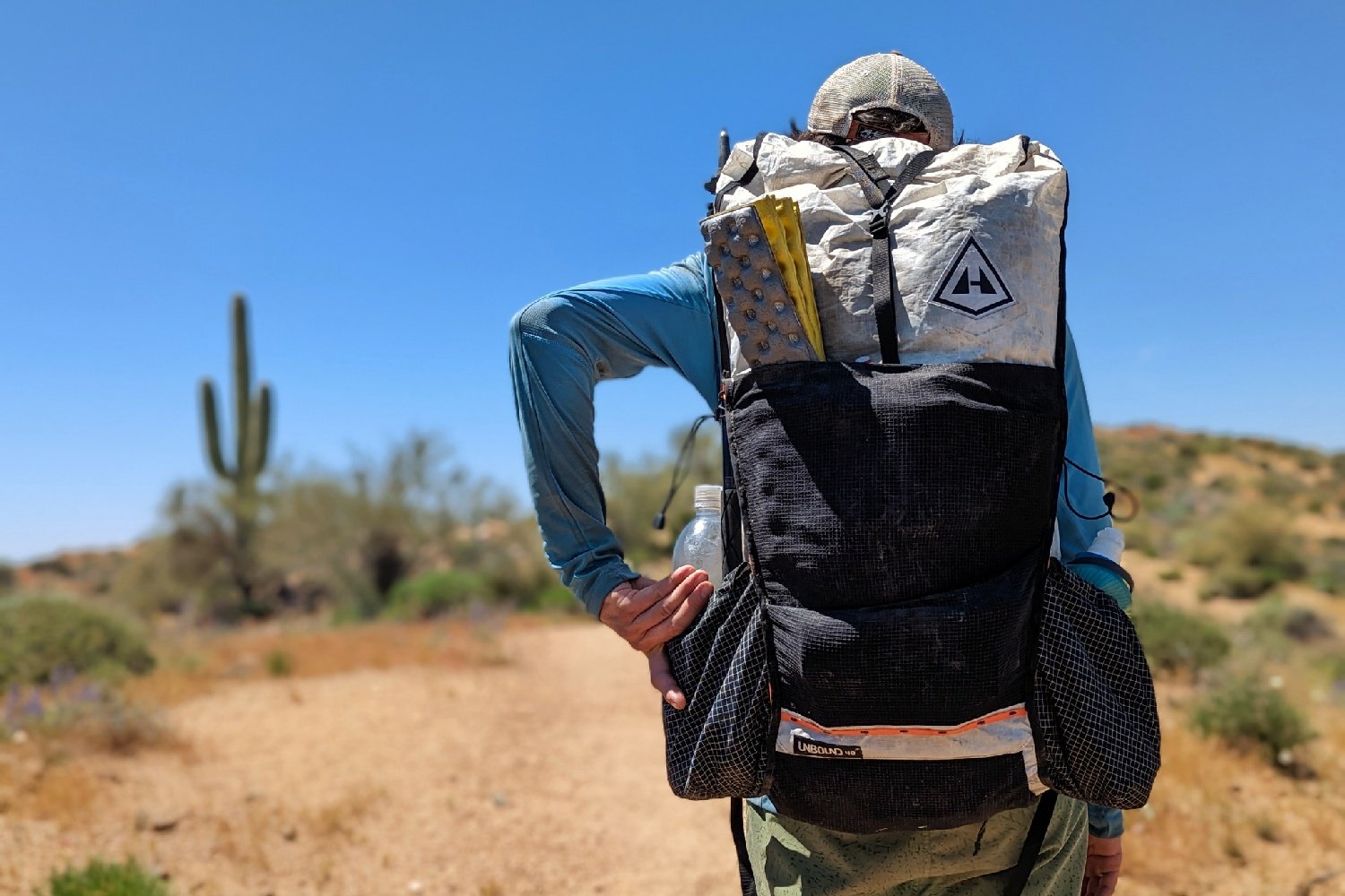 A hiker pulling a water bottle out of the side pocket on the Hyperlite Mountain Gear Unbound 40 - there is a tall saguaro cactus in the background
