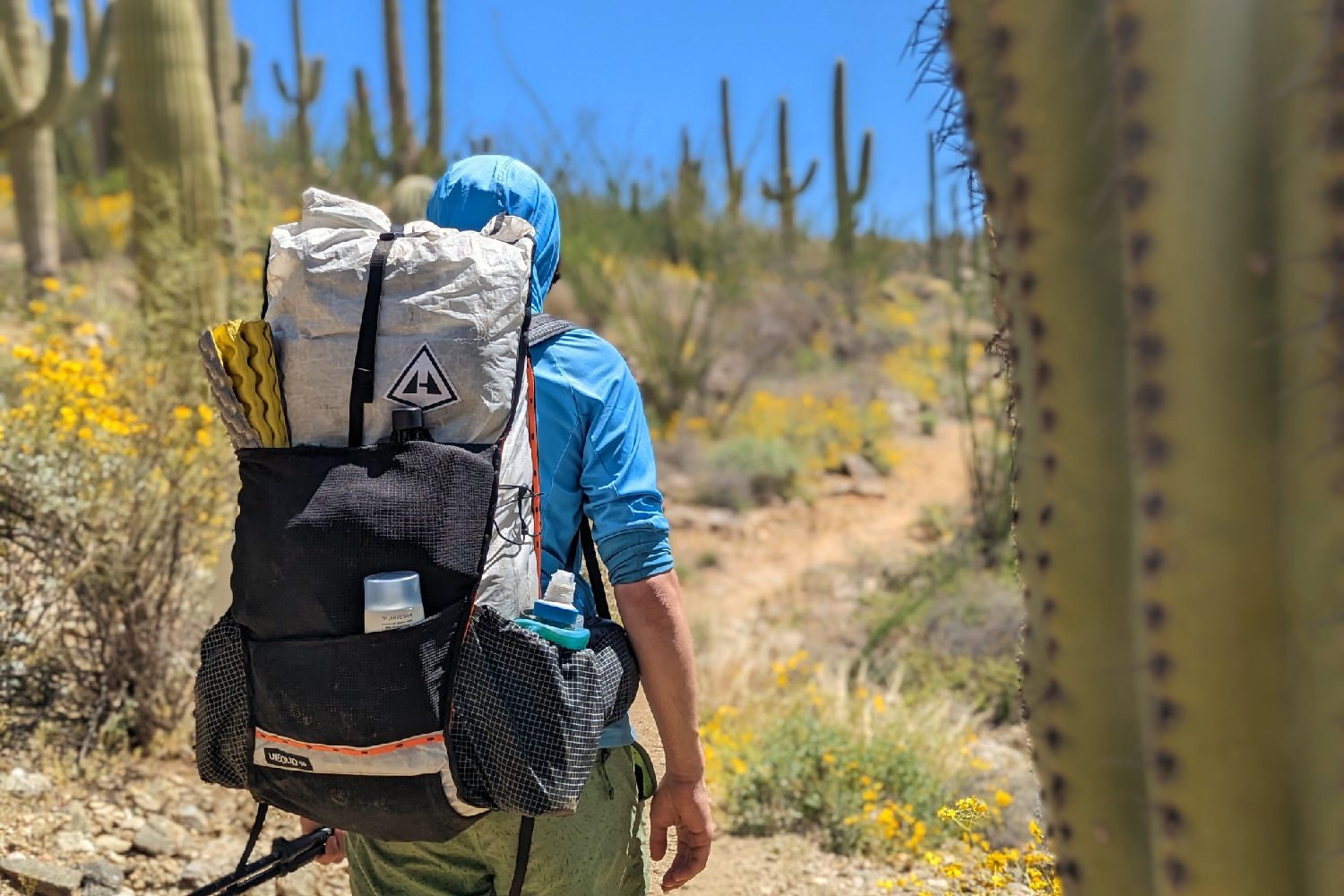 A hiker wearing the Hyperlite Mountain Gear Unbound 40 in Saguaro National Park - there is a blurred out cactus in the foreground and distant saguaros in the background