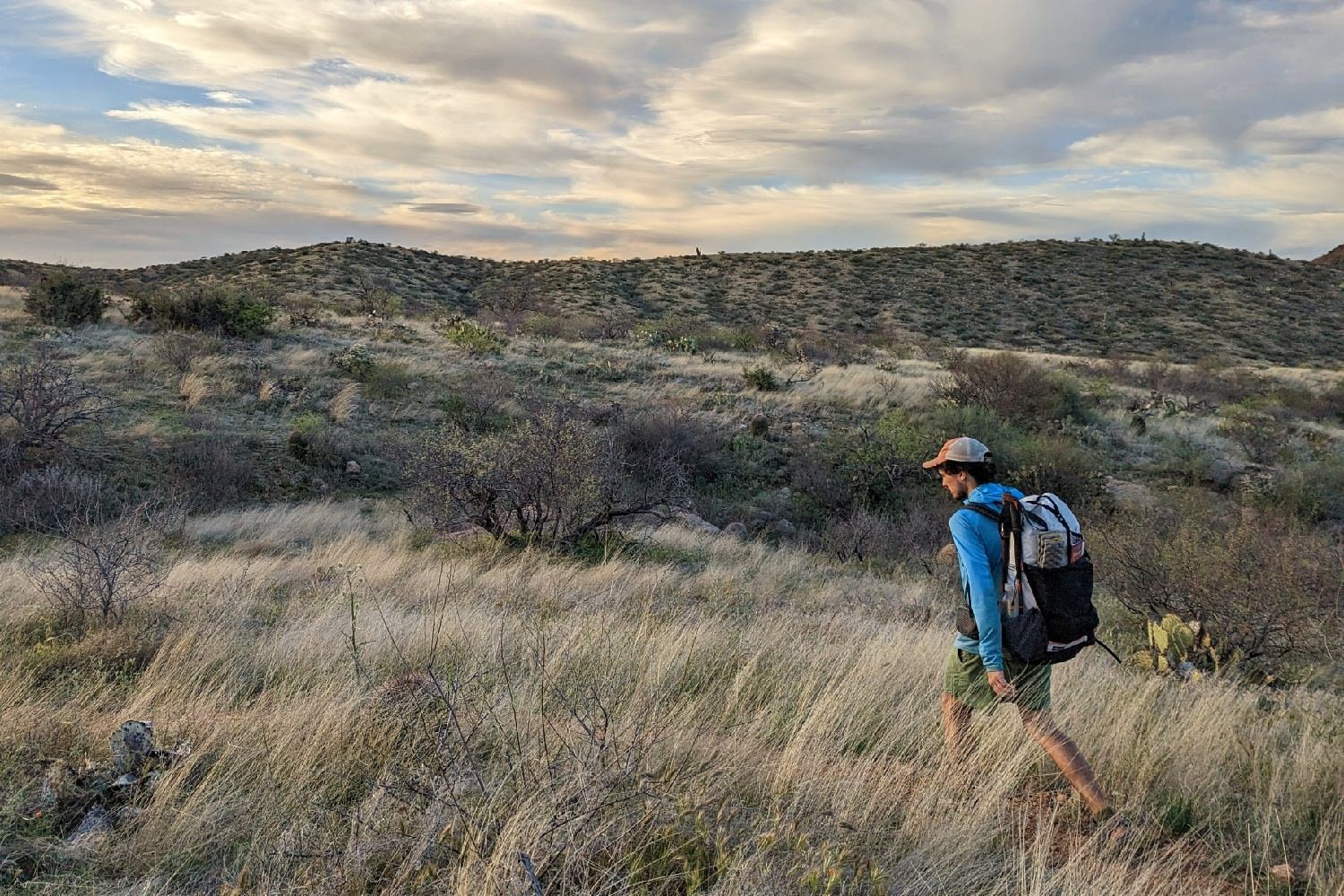 a side view of a hiker wearing the Hyperlite Mountain Gear Unbound 40 walking on a desert trail through some waving grass