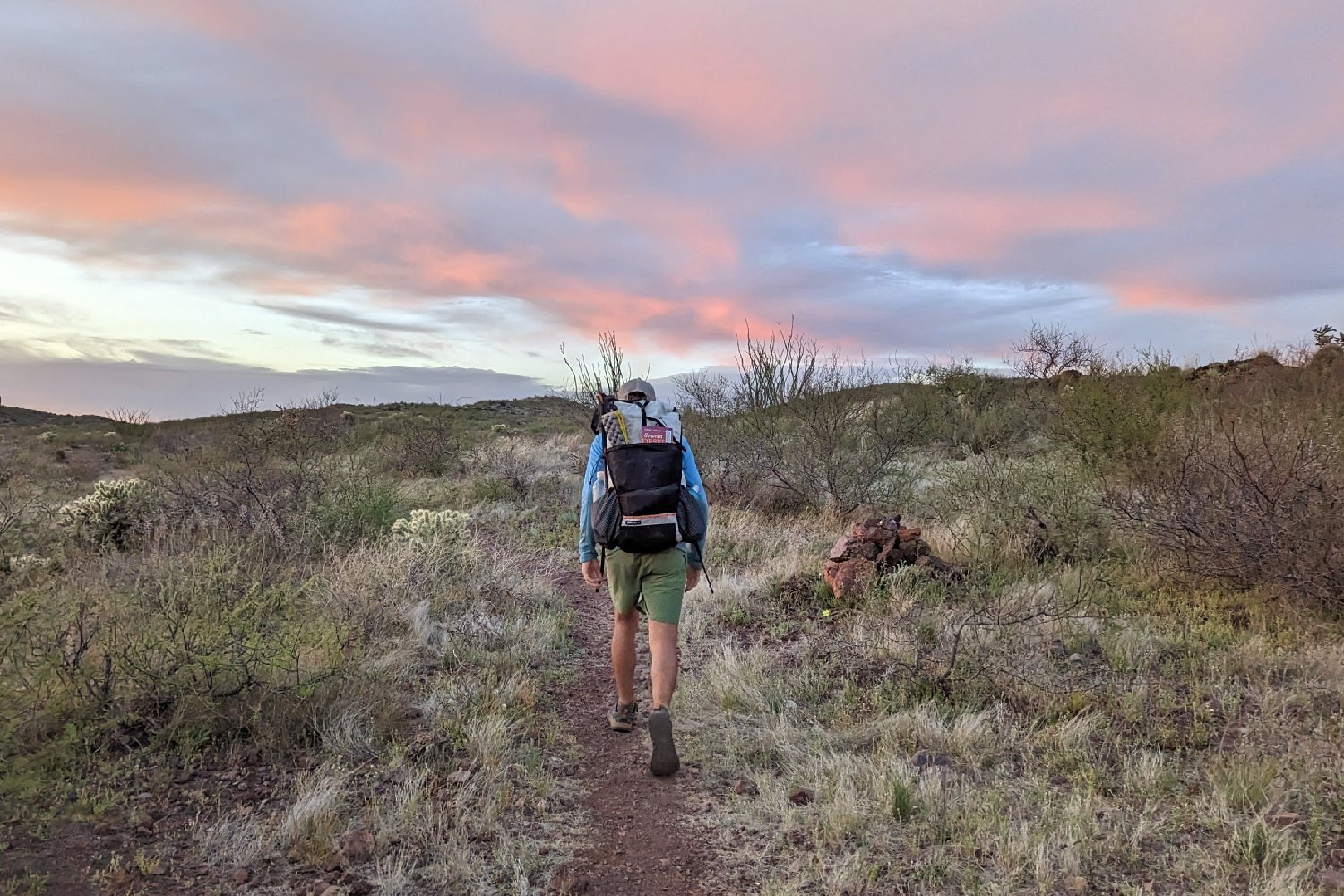 a hiker wearing the Hyperlite Mountain Gear Unbound 40 hiking away on a desert trail toward a pink sunset